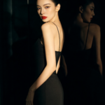 Elegant woman in black dress with red lipstick looking over shoulder.